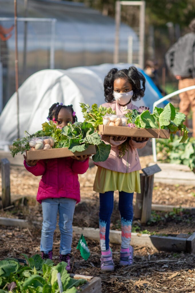 Two girls holding vegetables at Briggs Avenue Community Garden
